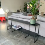 Zwart stalen sidetable met verbonden poten achter de bank