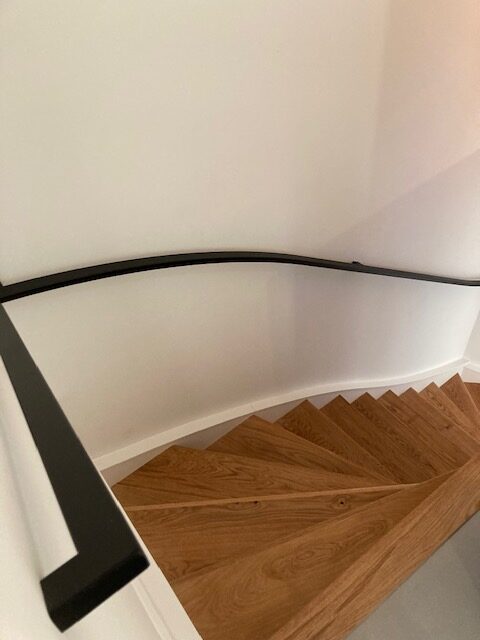 Gebogen design trapleuning, gemaakt van staal en zwart gepoedercoat bij houten trap
