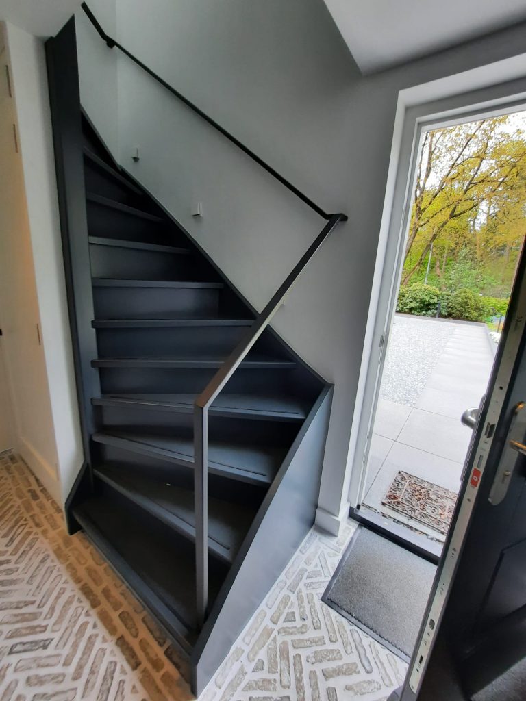 Zwarte doorlopende trapleuning met open balustrade bij een hoektrap dubbele kwart draai