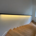 Zwarte stalen design trapleuning met ledverlichting, hangt bij eikenhouten trap. Trap met een raam