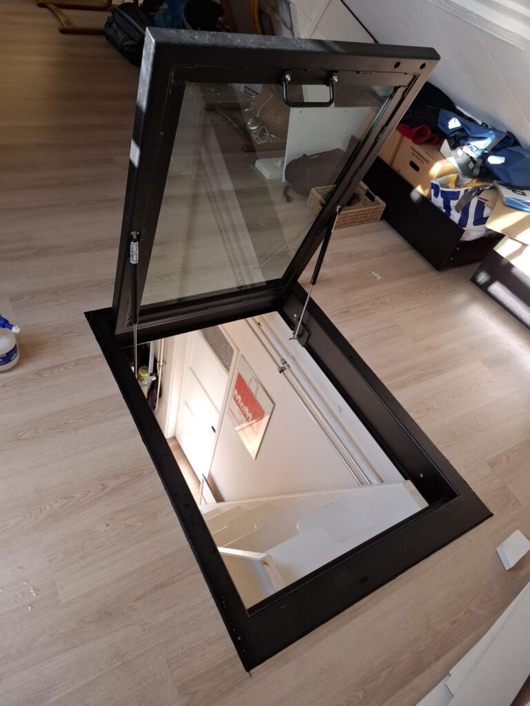 zwart stalen vloerluik met gasveren op zolder met beloopbaar glas